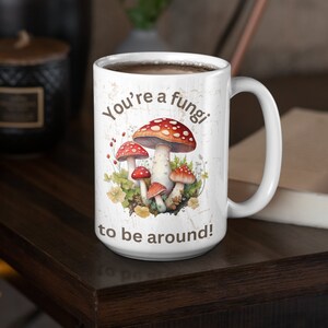 May include: White ceramic coffee mug with a brown and white design featuring mushrooms and the text "You're a fungi to be around!"