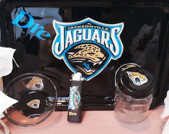 Op de afbeelding: Zwarte roltafel met een Jacksonville Jaguars logo, een kleine glazen kom, een glazen pot met deksel en een aansteker. De tafel, kom, pot en aansteker hebben allemaal het Jaguars logo.
