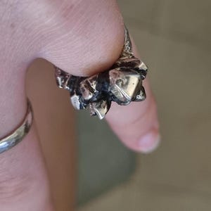 May include: A silver ring with a textured, crystal-like design. The ring is worn on a finger.