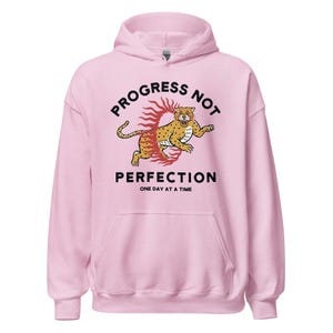 light pink Hoodie with the phrase "Progress Not Perfection," a popular recovery and 12 step slogan used in AA and NA.