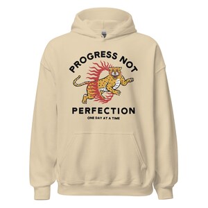 sand Hoodie with the phrase "Progress Not Perfection," a popular recovery and 12 step slogan used in AA and NA.