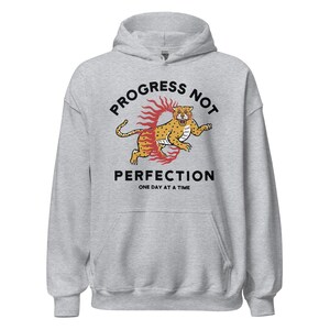 heather grey Hoodie with the phrase "Progress Not Perfection," a popular recovery and 12 step slogan used in AA and NA.