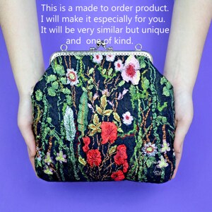 May include: A black fabric clutch purse with a floral embroidery design. The embroidery features red, pink, and white flowers with green leaves. The purse has a silver clasp.