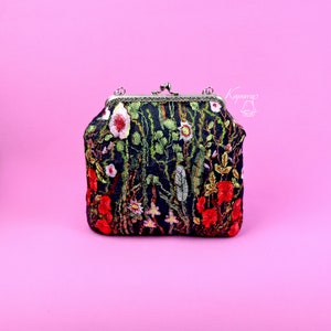 May include: A black velvet clutch bag with a floral embroidery design featuring red, pink, and green flowers. The bag has a silver clasp and a chain strap.