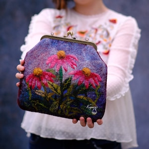 May include: A purple felt clutch bag with a floral design featuring pink and yellow flowers. The bag has a metal clasp and a small metal tag with the word "Kraynvy" on it.