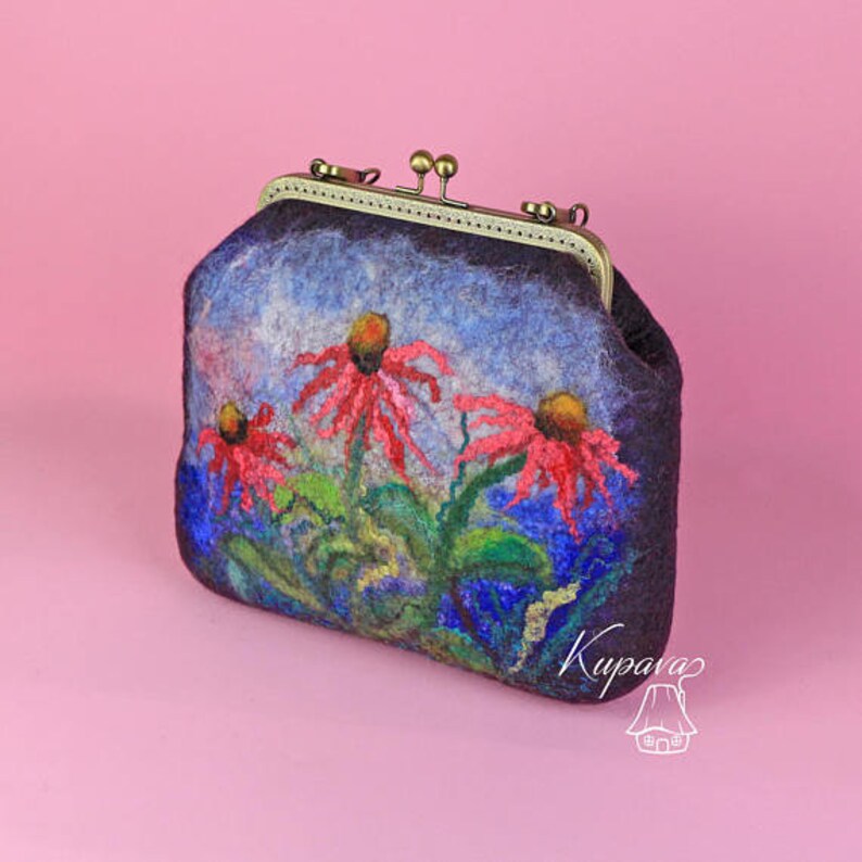 May include: A small, dark blue felt clutch bag with a floral design. The flowers are red, pink, and yellow, and they are painted on the front of the bag. The bag has a brass clasp and a small, silver tag with the word "Kupava" on it.