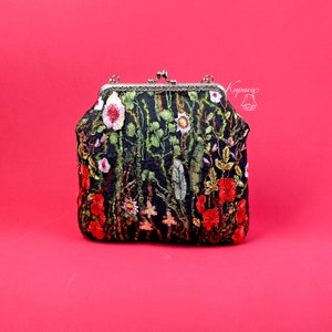 May include: A black fabric clutch purse with a floral embroidery design featuring red, pink, and green flowers. The purse has a silver clasp and a silver chain strap.