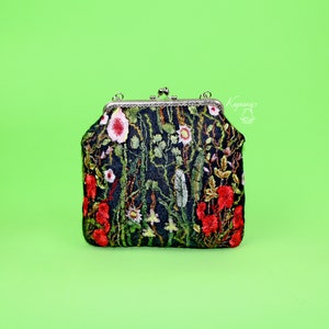 May include: A black velvet clutch purse with a floral embroidery design featuring red, pink, and green flowers. The purse has a silver clasp and a chain strap.