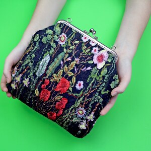 May include: A black velvet clutch purse with a floral embroidery design featuring red, pink, and green flowers. The purse has a silver clasp.