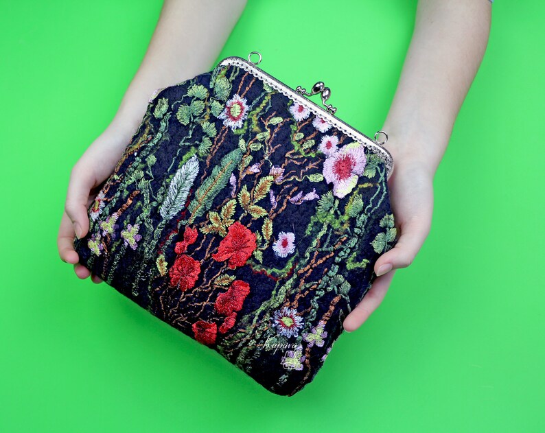 May include: A black velvet clutch purse with a floral embroidery design featuring red, pink, and green flowers. The purse has a silver clasp.