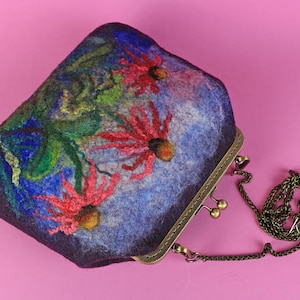 May include: A purple felt clutch bag with a floral design featuring red, green and blue flowers. The bag has a brass clasp and a chain strap.