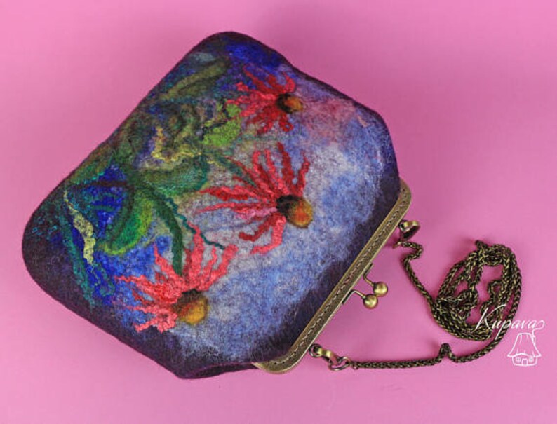 May include: A purple felt clutch bag with a floral design featuring red, green and blue flowers. The bag has a brass clasp and a chain strap.