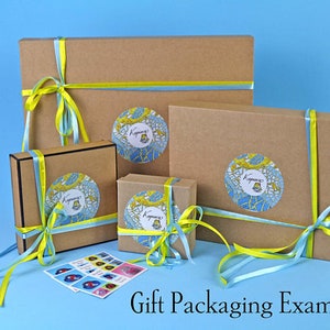 May include: Gift packaging example showing three brown cardboard boxes with yellow and blue ribbon tied around them. Each box has a colorful sticker with a design and the word "Kyivana" on it.