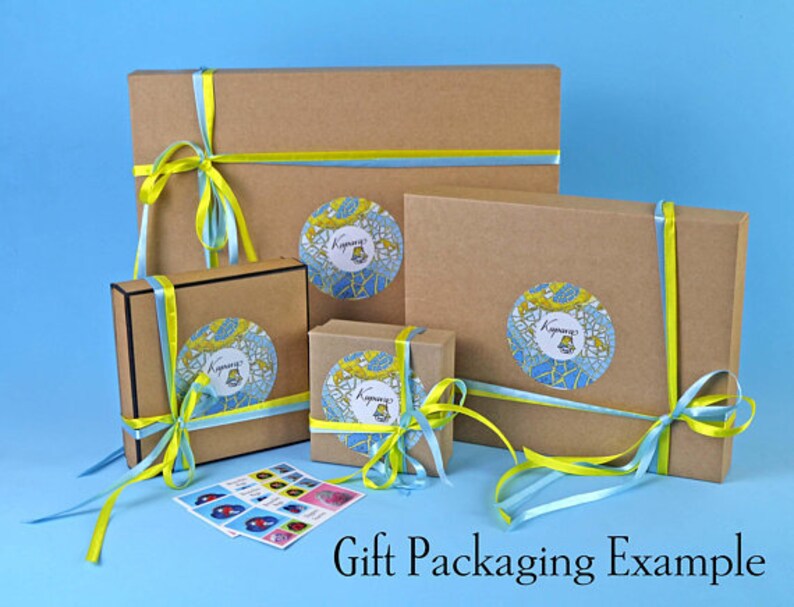 May include: Gift packaging example showing three brown cardboard boxes with yellow and blue ribbon tied around them. Each box has a colorful sticker with a design and the word "Kyivana" on it.