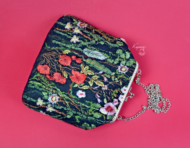 May include: A black velvet clutch bag with a floral embroidery design featuring red, green, and white flowers. The bag has a silver chain strap and a silver clasp.