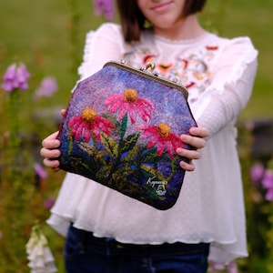 May include: A purple felt clutch bag with a floral design featuring pink and yellow flowers. The bag has a metal clasp and the text "Kayana" is embroidered on the front.