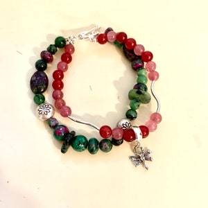May include: Two layered beaded bracelets. The bracelets feature a variety of colorful beads in shades of red, pink, green, and purple. Silver-toned accents include a dragonfly charm and flower-shaped beads.