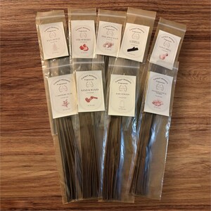May include: Assortment of 10 packs of incense sticks in clear plastic packaging. Each pack has a label with the name of the scent, such as "Patchouli", "Strawberry", "Pineapple Sage", "Sandalwood", "Baby Powder", and "Frankincense & Myrrh".