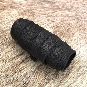 Op de afbeelding: Een opgerolde strook zwart leer, met een getextureerd oppervlak. Het leer lijkt dik en duurzaam, met een lichte glans. De achtergrond is een lichtbruine, harige textuur.