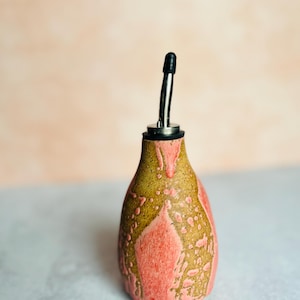 Può includere: Una bottiglia di ceramica rosa e marrone per olio e aceto con un beccuccio in acciaio inossidabile.