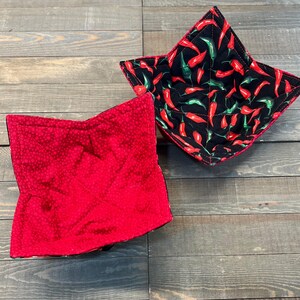 May include: Two quilted fabric bowl cozies. One is red with white polka dots and the other is black with a red and green chili pepper pattern.