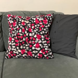 May include: Two throw pillows on a green couch. One pillow has a black, white, and pink geometric pattern. The other pillow is solid black.