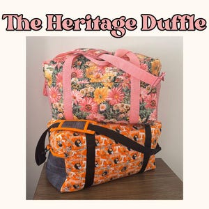 May include: Two duffle bags stacked on a wooden surface. The top bag has a floral pattern with pink straps. The bottom bag is orange with a repeating dog graphic and black straps. Text at the top reads "The Heritage Duffle."