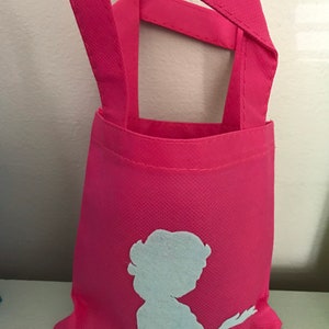 Puede incluir: Una bolsa de tela reutilizable de color rosa con una silueta blanca de una mujer en la parte delantera.
