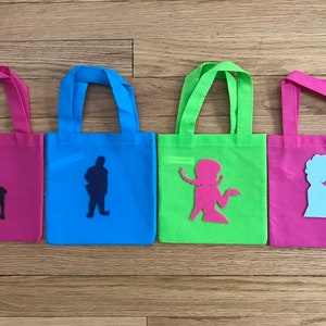 Puede incluir: Cuatro peque&ntilde;as bolsas de mano con diferentes telas de colores y siluetas de personajes. Las bolsas son rosa, azul, verde y rosa. Los personajes son un reno, un hombre, una mujer y una mujer.
