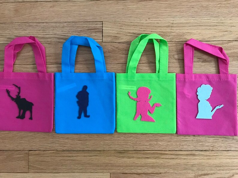 Puede incluir: Cuatro peque&ntilde;as bolsas de mano con diferentes telas de colores y siluetas de personajes. Las bolsas son rosa, azul, verde y rosa. Los personajes son un reno, un hombre, una mujer y una mujer.