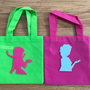 Puede incluir: Dos peque&ntilde;as bolsas de mano verde y rosa con recortes de tela de mujeres en silueta. La bolsa verde tiene un recorte rosa y la bolsa rosa tiene un recorte azul claro.