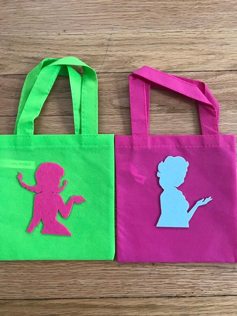 Puede incluir: Dos peque&ntilde;as bolsas de mano verde y rosa con recortes de tela de mujeres en silueta. La bolsa verde tiene un recorte rosa y la bolsa rosa tiene un recorte azul claro.