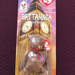 以下が含まれることがあります： 赤いリボンと小さなイギリス国旗をつけた茶色のビーニーベイビーのクマ。クマは、タイのタグとロンドンのビッグベンを背景にした画像が付いたビニール袋に入っています。パッケージには、「Collect All 4! While supplies last.」と「Britannia The Bear」のテキストも含まれています。