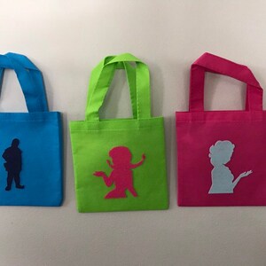 Puede incluir: Tres peque&ntilde;as bolsas de mano con diferentes telas de colores y siluetas. La bolsa de la izquierda es azul con una silueta azul oscuro de una persona. La bolsa del medio es verde con una silueta rosa de una persona. La bolsa de la derecha es rosa con una silueta azul claro de una persona.