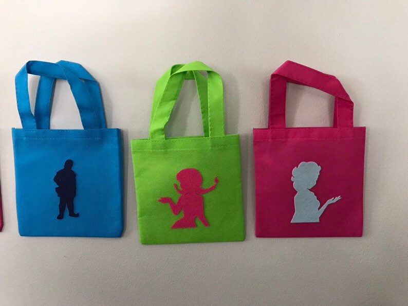Puede incluir: Tres peque&ntilde;as bolsas de mano con diferentes telas de colores y siluetas. La bolsa de la izquierda es azul con una silueta azul oscuro de una persona. La bolsa del medio es verde con una silueta rosa de una persona. La bolsa de la derecha es rosa con una silueta azul claro de una persona.