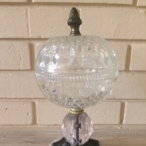 May include: A clear glass globe with a cut glass design sits on a pink glass base with a metal and marble base. The globe has a small metal finial on top.