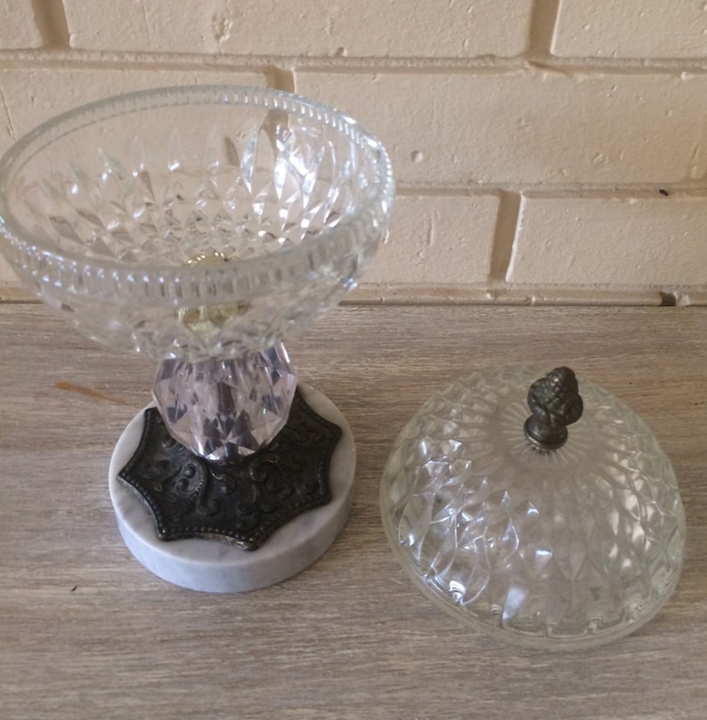 May include: A clear glass candy dish with a diamond pattern and a marble base. The dish has a lid with a small knob on top.