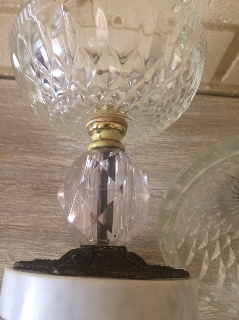 May include: A clear glass pedestal with a diamond pattern, a gold-colored base, and a white marble base.