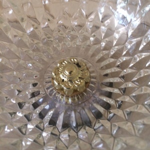 May include: Close-up of a gold-colored metal ceiling fixture with a decorative floral design. The fixture is surrounded by a clear, textured glass.