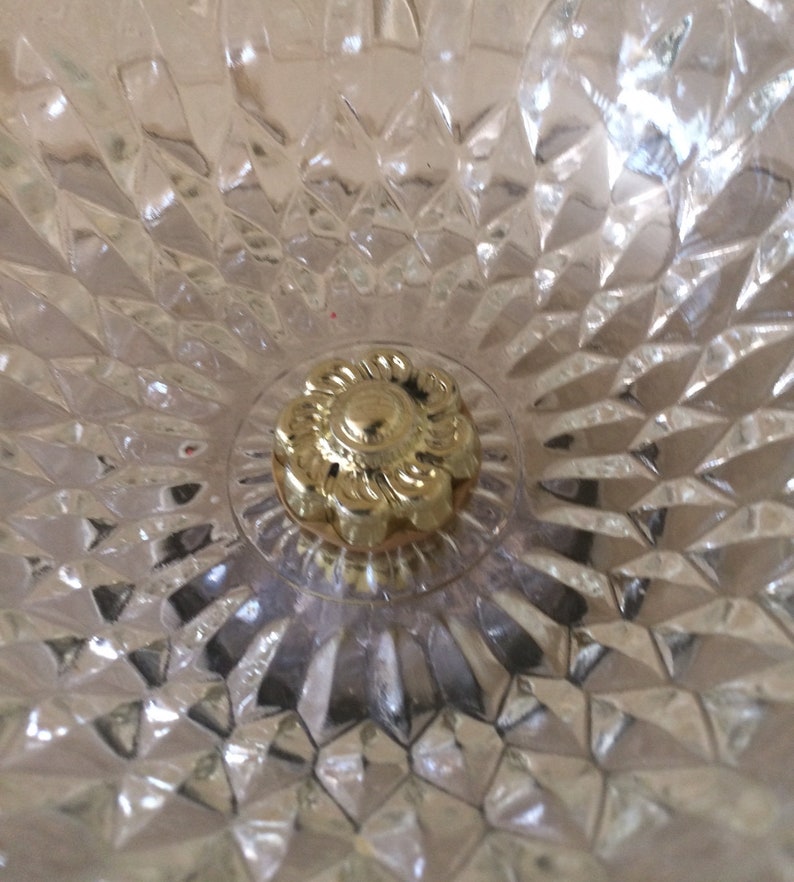 May include: Close-up of a gold-colored metal ceiling fixture with a decorative floral design. The fixture is surrounded by a clear, textured glass.