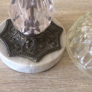 May include: A vintage table lamp with a clear glass shade and a crystal base. The base is mounted on a marble platform with an ornate metal trim.
