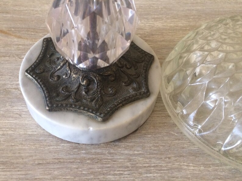 May include: A vintage table lamp with a clear glass shade and a crystal base. The base is mounted on a marble platform with an ornate metal trim.