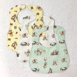 May include: Three baby bibs featuring Winnie the Pooh and friends designs. One bib is yellow with a Winnie the Pooh and Tigger design, one is white with a Winnie the Pooh and Piglet design, and one is green with a Winnie the Pooh and Piglet design.