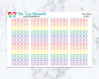 May include: A sheet of pastel-colored mood tracker stickers. Each sticker features a series of smiley faces and other expressions. The sheet is labeled "Mood Trackers in Pastel" and includes the logo for "The Twin Mermaids."
