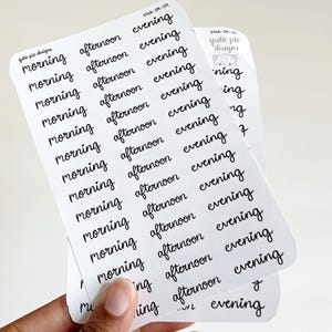 May include: Two white sticker sheets with black text. The stickers are labeled with the words "morning," "afternoon," and "evening." The stickers are from "qutie pie designs."