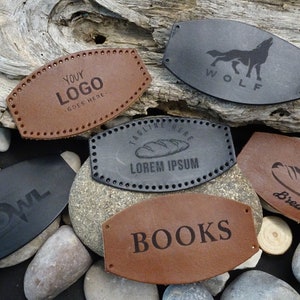 Peut inclure: Six étiquettes en cuir différentes avec divers motifs et textes. Les étiquettes sont brunes et noires et ont un bord cousu. Les motifs comprennent un loup, une miche de pain, un hibou, les mots "Your Logo", "Books" et "Lorem Ipsum".