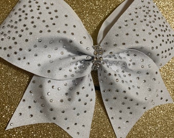 May include: A white cheer bow with silver glitter and rhinestones. The bow is tied with a white ribbon.