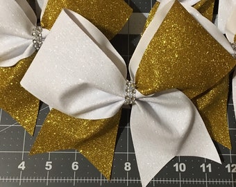 May include: Four white and gold glitter cheer bows with rhinestones in the centre. The bows are approximately 15 cm wide.