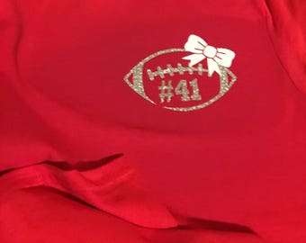 May include: Red t-shirt with a silver glitter football design and a white bow. The football has the number 41 on it.