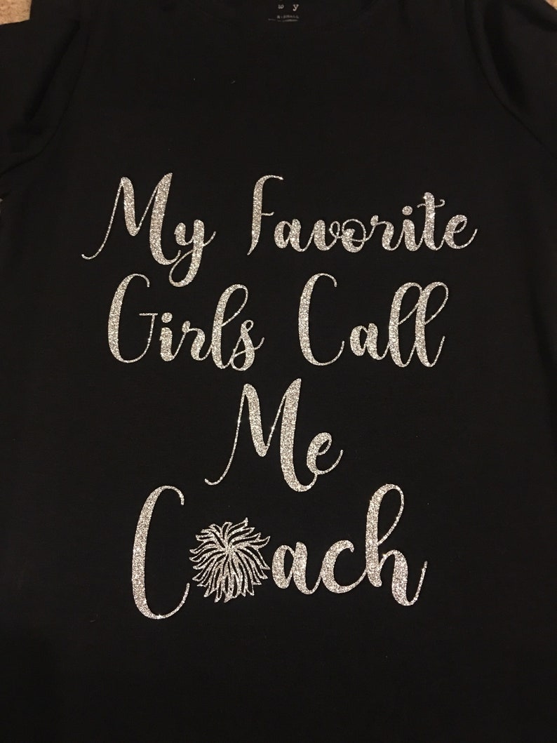 May include: Black t-shirt with silver glitter lettering that reads "My Favourite Girls Call Me Coach" with a silver glitter pom-pom.